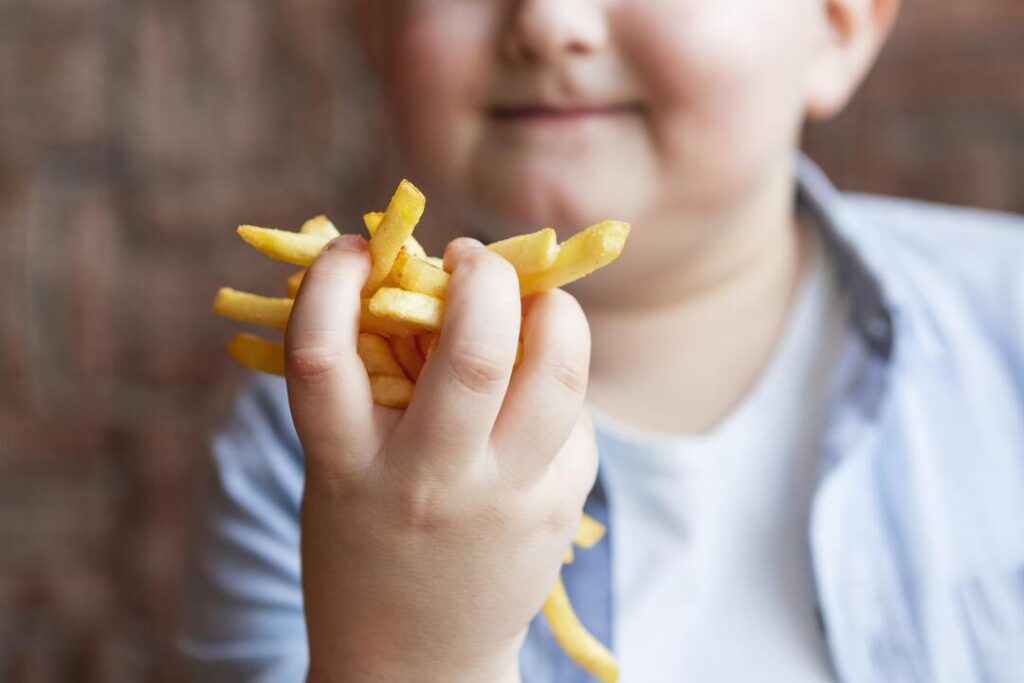 Criança comendo alimentos que podem causar obesidade infantil.